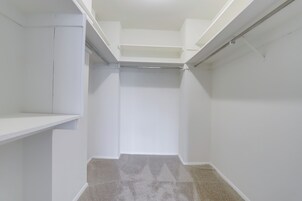 Un armario estrecho, con paredes blancas y piso alfombrado.