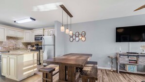 Una cocina moderna con una isla central, bancos de madera, iluminación colgante y un televisor de pantalla plana montado en la pared.
