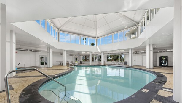 Piscina interior con vista despejada al cielo a través de amplios ventanales, rodeada de paredes y columnas blancas.