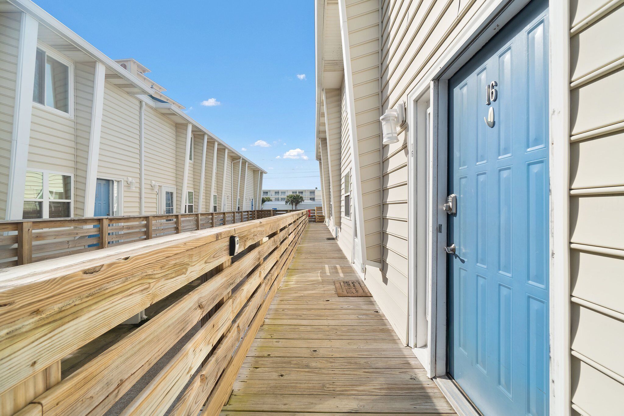 A wooden boardwalk leading to a building with a blue door, white siding, and a clear sky.