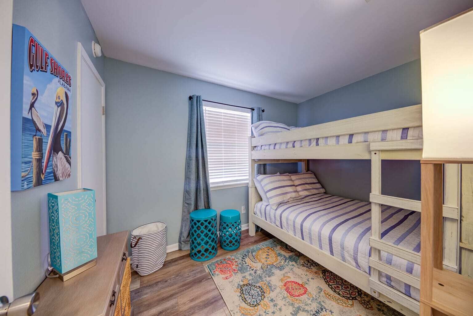 Una habitación pequeña y acogedora con una cama litera, un cartel en la pared, una mesita y una alfombra estampada.