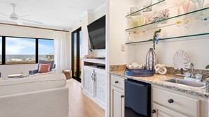 A modern kitchen with a large window, a built-in TV, and a glass display shelf with decorative items. - ☀️Ground Floor Condo w/Pool & Lawn-Four Seasons-103E☀️ (Orange Beach)
