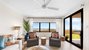 A spacious living room with a ceiling fan, two grey armchairs, a white sofa, and a large window offering a view of the outdoors. - ☀️Ground Floor Condo w/Pool & Lawn-Four Seasons-103E☀️ (Orange Beach)