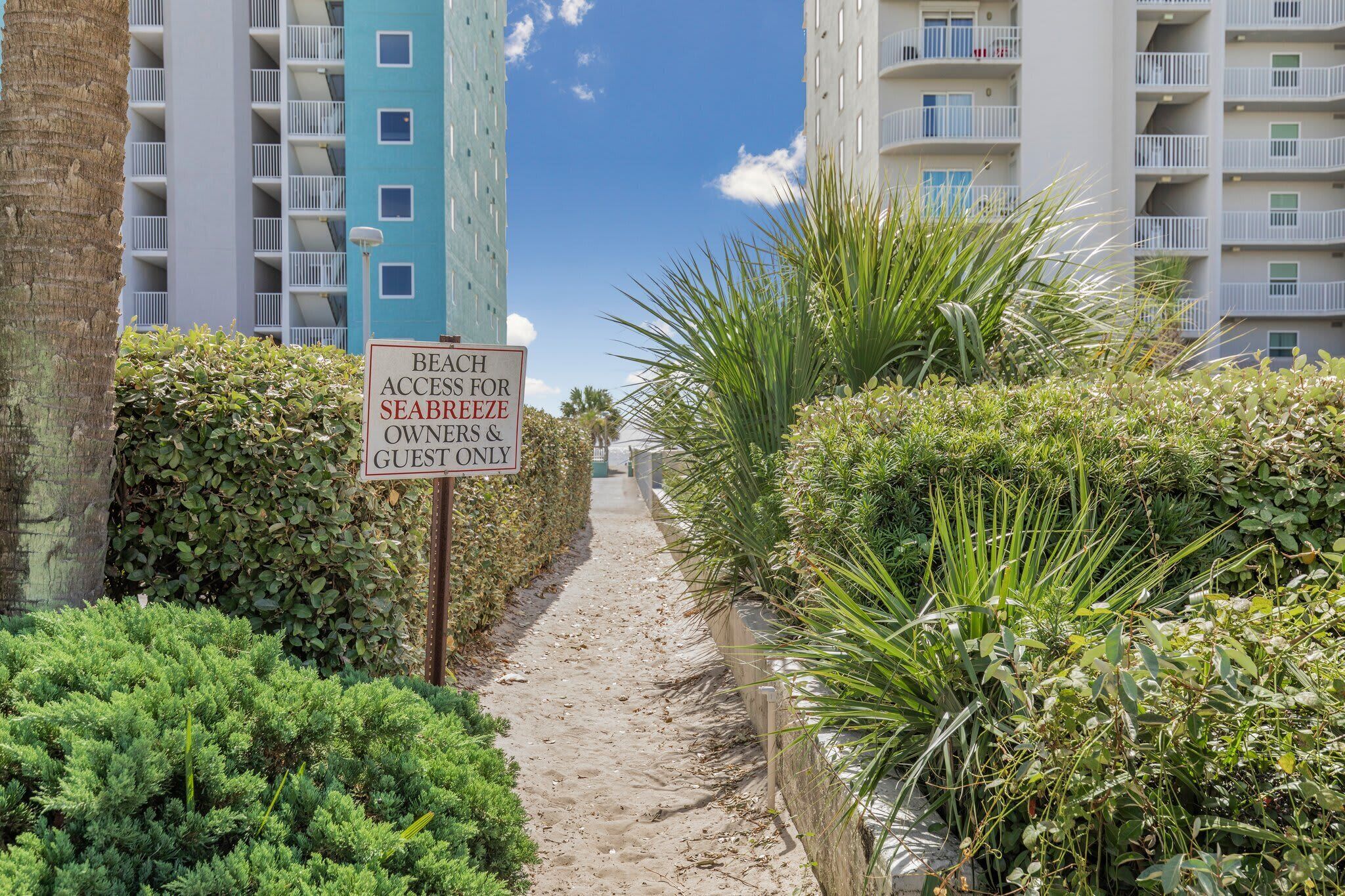 A pathway leading to a beachfront property with a sign indicating beach access for owners and guests.