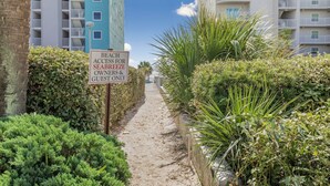 Un sendero que conduce a una propiedad frente al mar, con un letrero que indica acceso a la playa para propietarios e invitados.