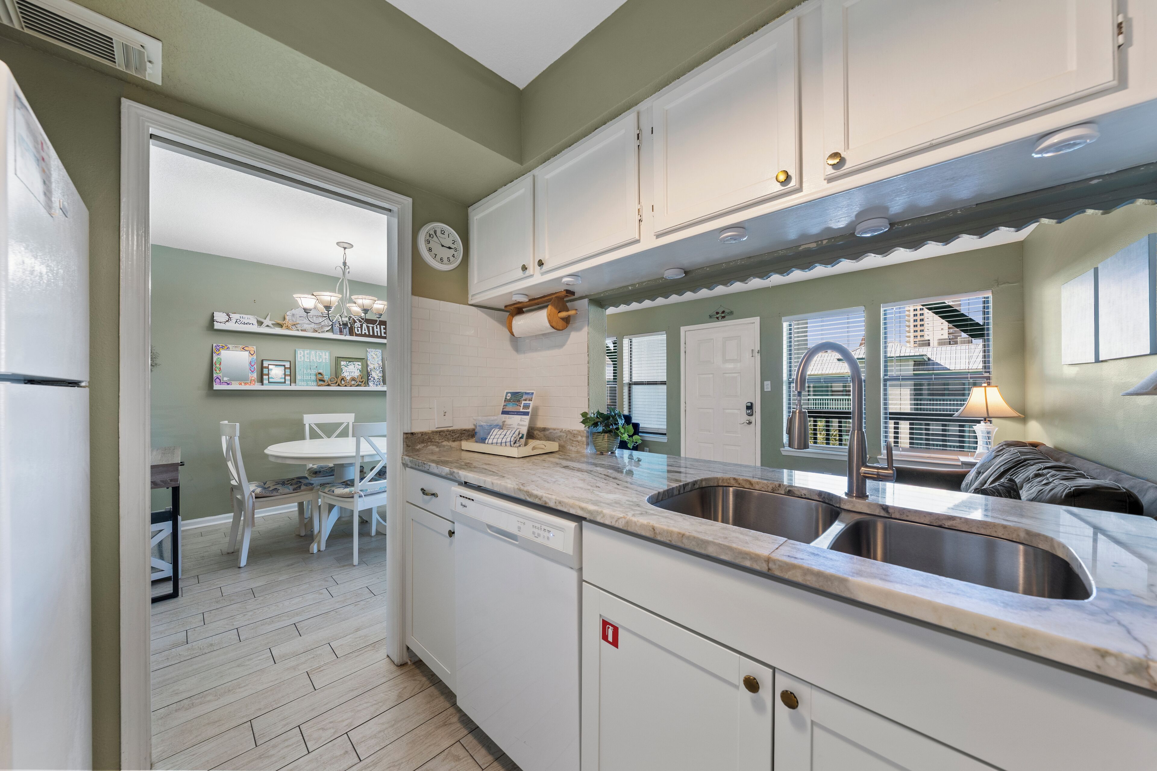 Een keuken met witte kastjes, een roestvrijstalen spoelbak en een eethoek met een witte tafel en stoelen.