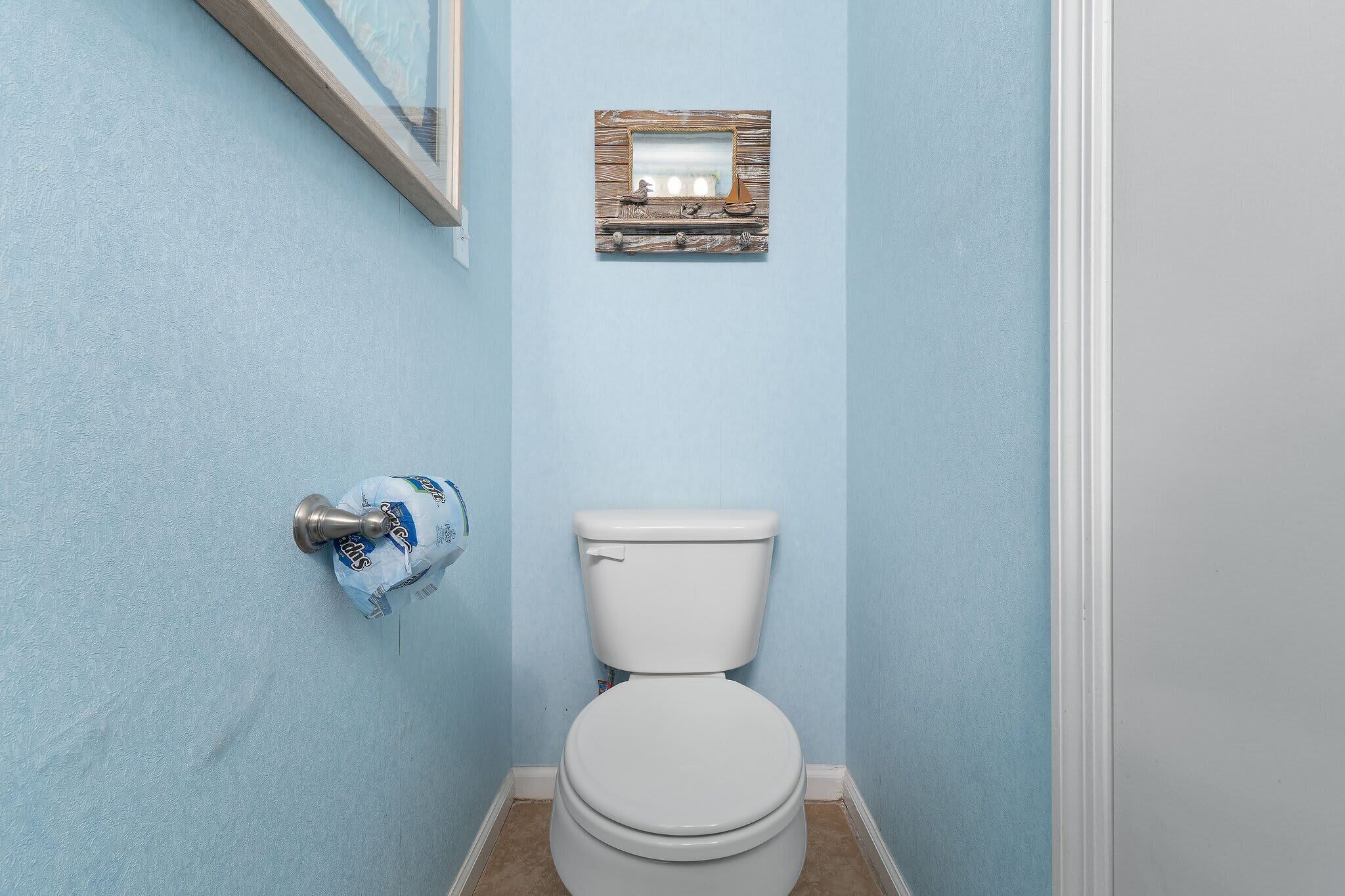 Un baño con inodoro, dispensador de toallas y un pequeño espejo con marco de madera en la pared.