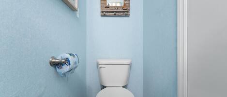 Un baño con inodoro, dispensador de toallas y un pequeño espejo con marco de madera en la pared.
