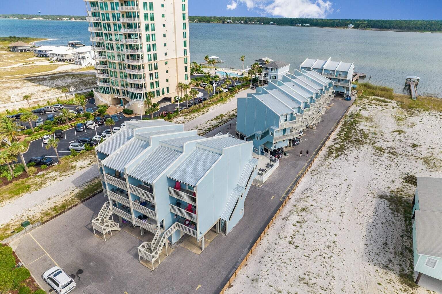 Un hotel frente a la playa con varias construcciones, un estacionamiento y vista al océano.
