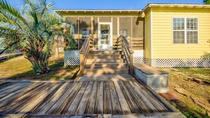 A wooden deck leading to a yellow house with a door and windows, surrounded by a fence and palm trees. - 🌞Beach Cottage in Ft Morgan-Pool-The Rookery 2202🌞 (Gulf Shores)