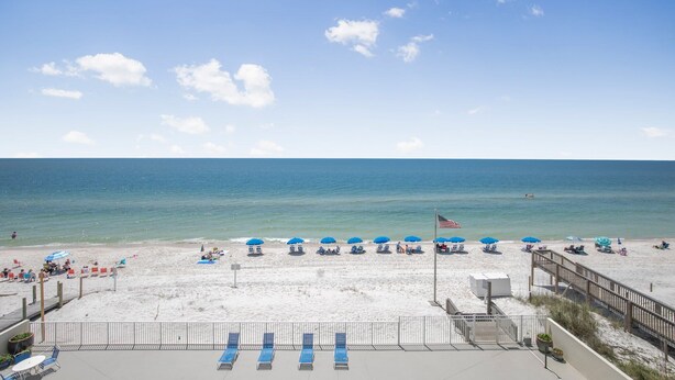 Ein Strand mit blauen Sonnenschirmen, Liegestühlen und einer Holzpromenade.