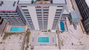 Ein Hochhaus-Hotel mit mehreren Balkonen, zwei Swimmingpools und einem Strandbereich mit Liegestühlen.