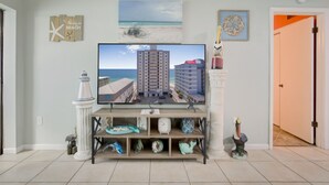 Ein Wohnzimmer mit einem Flachbildfernseher, der eine Strandansicht zeigt, einer kleinen Ablage mit Dekoration und einer Tür zu einem anderen Raum.