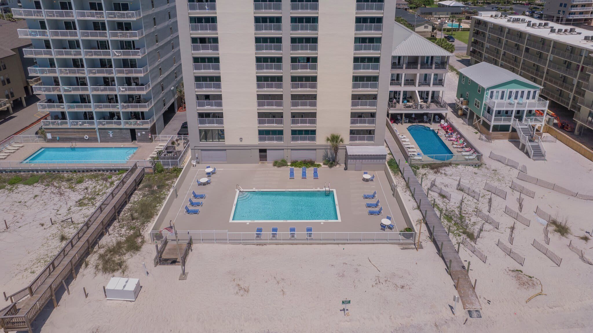 A hotel with a central swimming pool, multiple balconies, and a beach area.