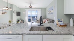 A modern kitchen with a granite countertop, white cabinets, a built-in dishwasher, and a ceiling fan.