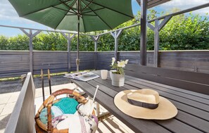 Relax on the patio with a comfortable bench and table, surrounded by lush greenery and a potted plant with white flowers.