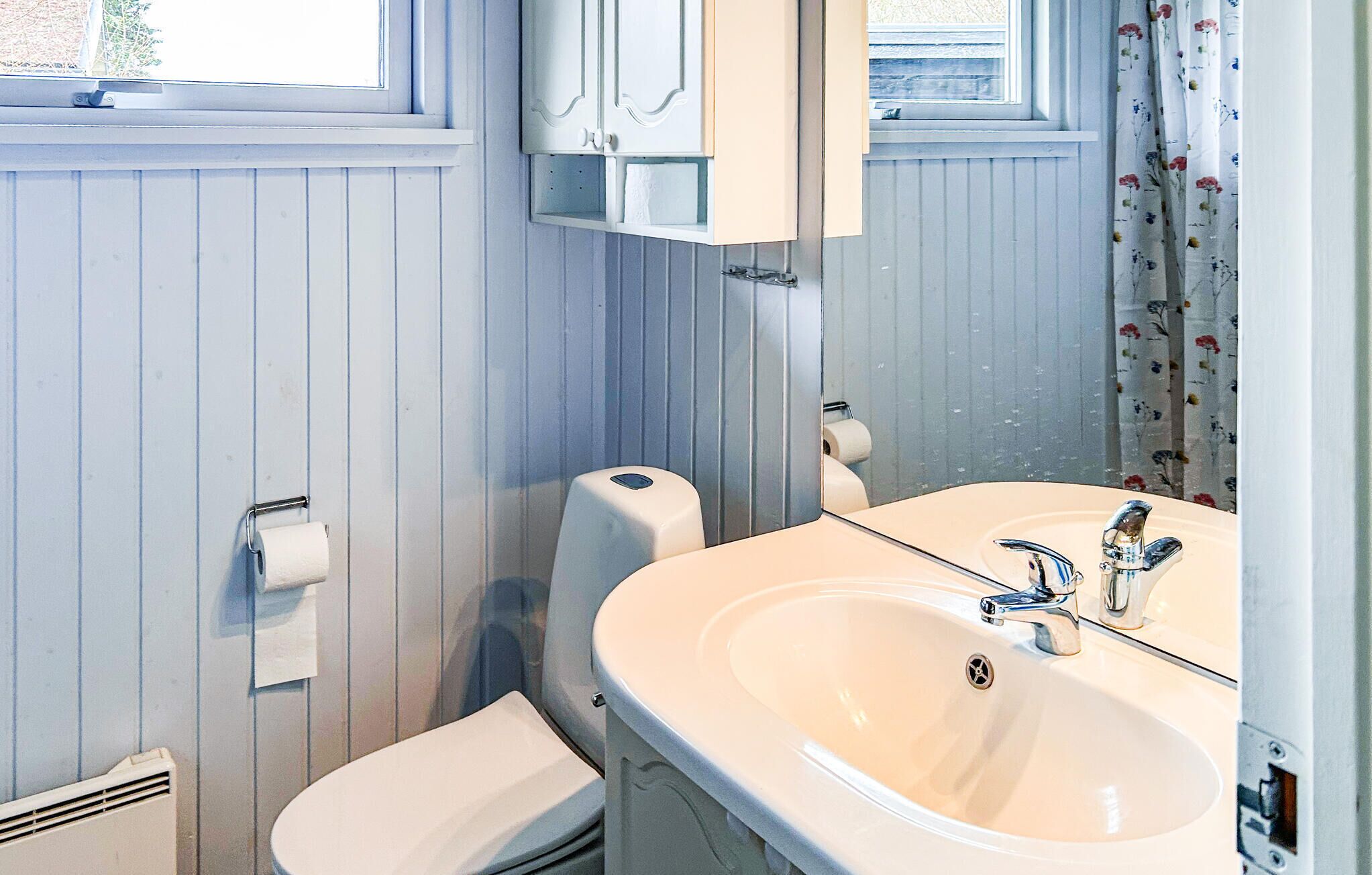 A bathroom with a white sink, mirror, toilet, and paper towel dispenser.
