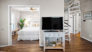 Un dormitorio con una cama, un televisor sobre un tocador blanco, una escalera y una puerta que da a otra habitación.