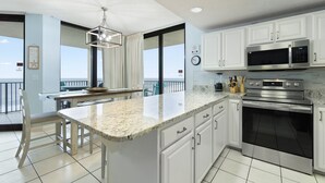A modern kitchen with white cabinets, a large island, stainless steel appliances, and a view to the outside.