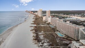 A coastal hotel with multiple high-rise buildings, a beach, and a swimming pool.