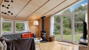 A cozy room with a sofa, a table with a plate of fruit, a fireplace, and large windows offering a view of the outdoors. - 3 bedroom lovely home in Nykøbing Sj (Nykøbing Sj)