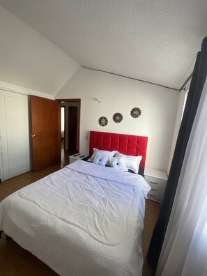 A bedroom with a red headboard, white bedding, and a wooden wardrobe. - Hostel Urban City Bogota (Bogotá)