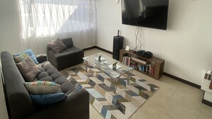 Una sala de estar con sofá, mesa de centro, televisor y estantería.