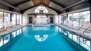 Une piscine intérieure avec des parois en verre transparent, un plafond en bois et des chaises longues disposées tout autour.