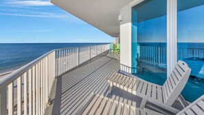 A balcony with a view of the ocean, a glass door leading to a pool, and a few chairs. - Views of beach w/ Two Pools-Lighthouse-918 (Gulf Shores)