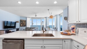 A modern kitchen with a large island, white cabinetry, and a view to the outside. - Views of beach w/ Two Pools-Lighthouse-918 (Gulf Shores)