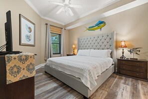 Une chambre avec un grand lit, un ventilateur de plafond, un tableau encadré, une table de chevet avec une lampe et un motif décoratif représentant des poissons sur le mur.