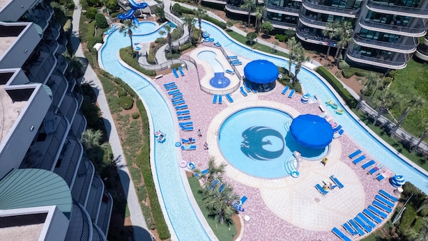 Un complejo turístico con varias piscinas, tumbonas y un edificio grande con balcones.