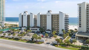 A multi-story hotel with a beach view, featuring a parking lot and palm trees.