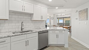 A modern kitchen with white cabinetry, a granite countertop, and a dishwasher.