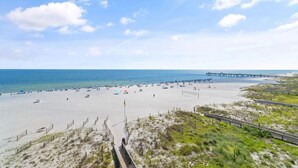A beach with a wooden boardwalk, a pier, and beach umbrellas.