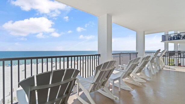 A balcony with white Adirondack chairs overlooking a beach.
