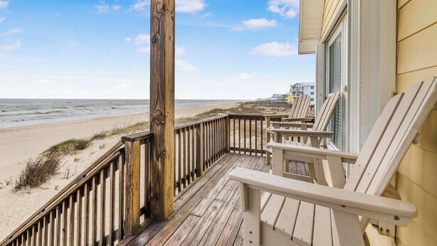 A wooden deck with beach views, a railing, and beach chairs.