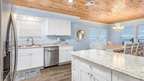 A modern kitchen with white cabinets, granite countertops, and a wooden ceiling.