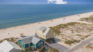 A beachfront property with a main house elevated on stilts, a smaller house, and a road leading to the beach.
