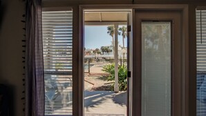 Vista a través de una puerta con un tapete estampado, que da a una zona de piscina con palmeras y una valla.