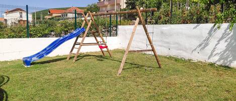 Une aire de jeux avec un toboggan bleu et deux balançoires.