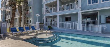 A pool area with blue lounge chairs, a small pool, and a multi-story building with balconies.