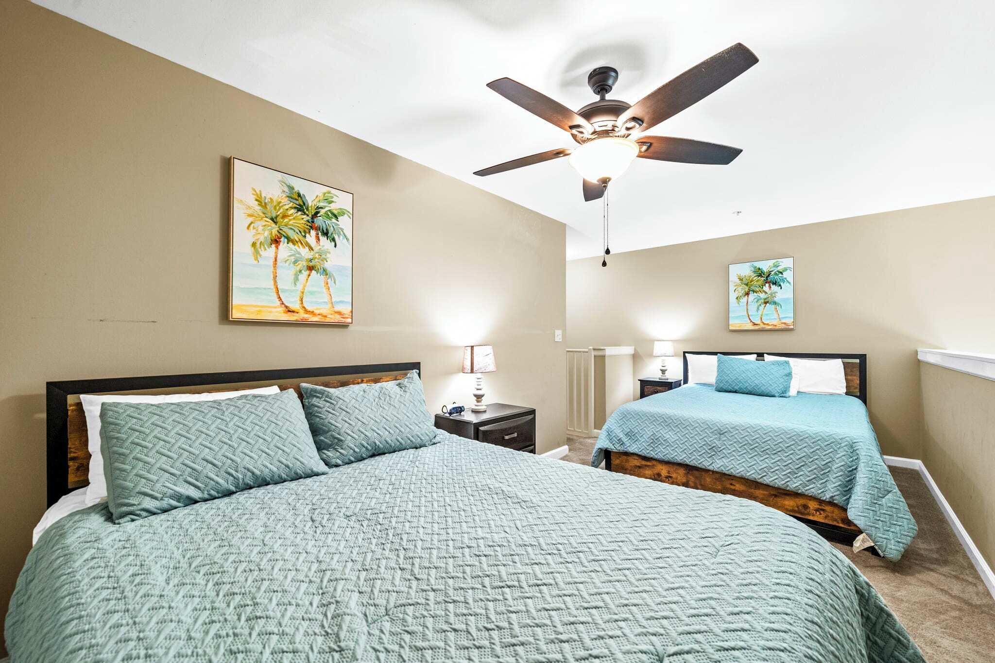 A bedroom with two beds, a ceiling fan, and artwork on the walls.
