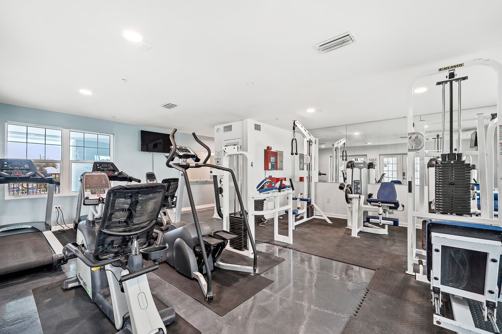 Ein modernes Fitnessstudio mit verschiedenen Trainingsgeräten, einem großen Fenster und einem Flachbildfernseher.
