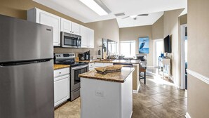A modern kitchen with stainless steel appliances, white cabinetry, and a granite countertop island.