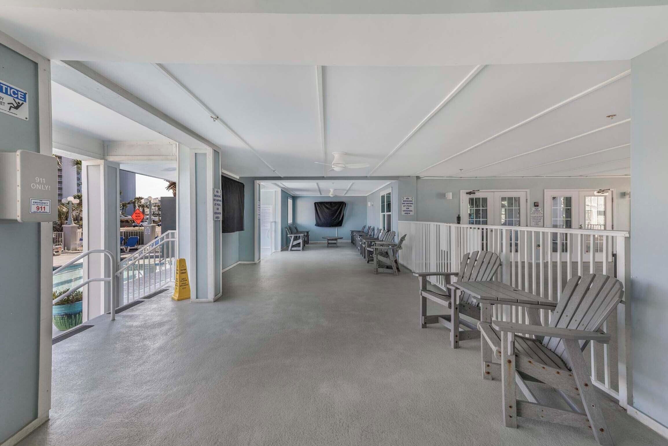 A spacious corridor with a ceiling fan, a seating area with wooden chairs, and a view of the outside.