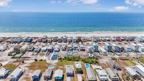 Vista aérea de una zona residencial costera con casas, algunas con piscinas, y una playa al fondo.
