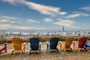 Ein Strand mit mehreren bunten Adirondack-Stühlen, die zum Meer hin ausgerichtet sind.