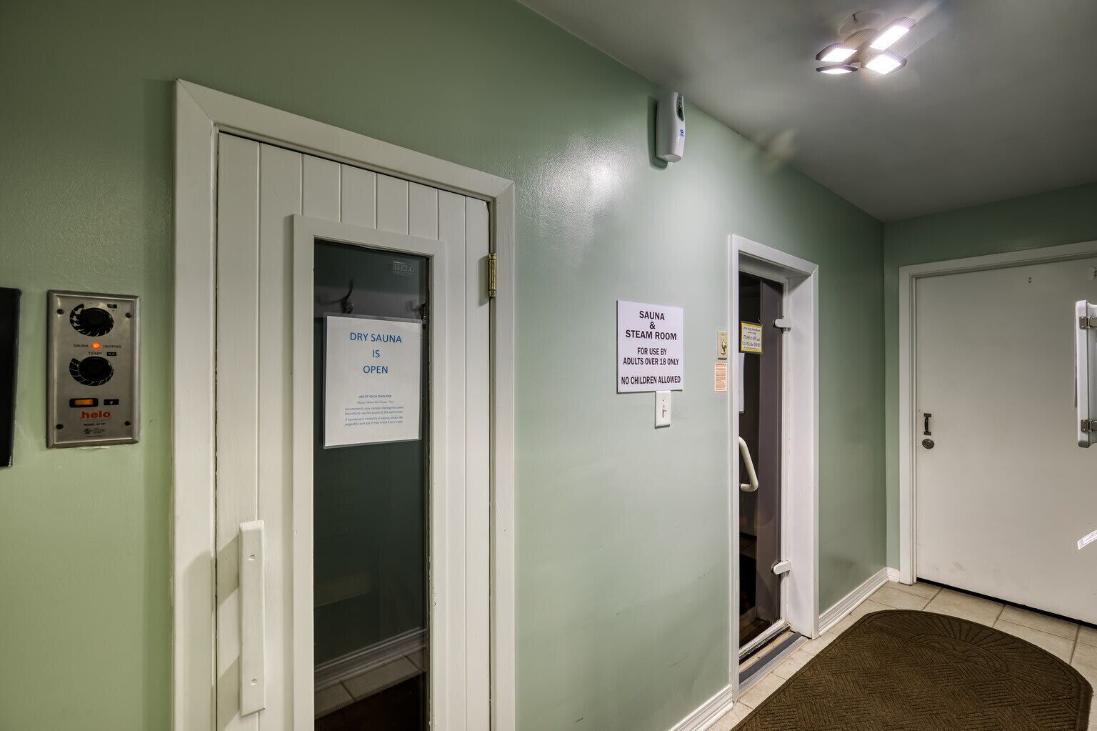 A hallway with a dry sauna sign, a sauna & steam room sign, and a thermostat on the wall.