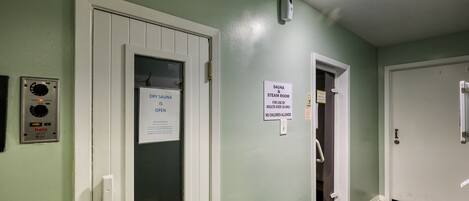 A hallway with a dry sauna sign, a sauna & steam room sign, and a thermostat on the wall.
